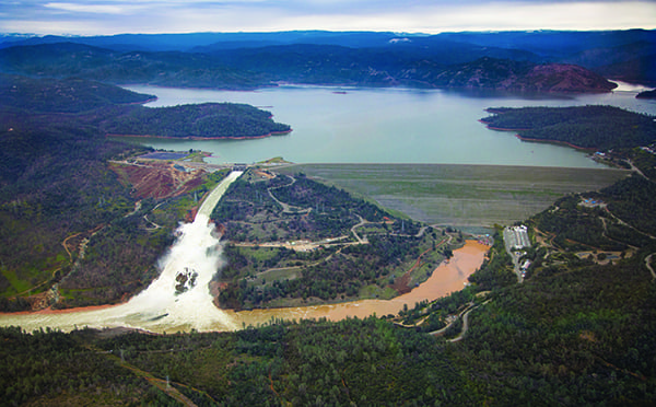 This aerial view looks east toward Oroville Dam and Lake Oroville, showing the damaged spillway with its outflow of 100,000 cubic feet per second (cfs) at the Butte County site. The California Department of Water Resources has a goal to lower the lake level by 50 feet to handle the next round of winter storms. Photo taken February 15, 2017. Dale Kolke / California Department of Water Resources