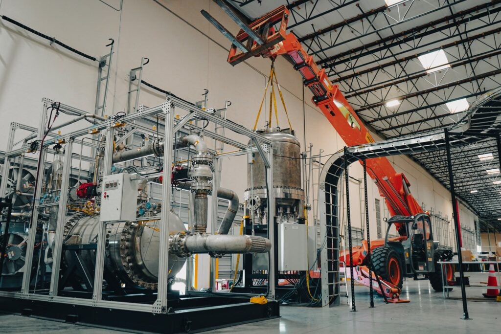 Industrial thermal testing equipment, stainless-steel piping, a large cylindrical vessel, and an orange telescopic lifting machine inside Antares Nuclear's Torrance facility.