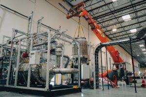 Industrial thermal testing equipment, stainless-steel piping, a large cylindrical vessel, and an orange telescopic lifting machine inside Antares Nuclear's Torrance facility.
